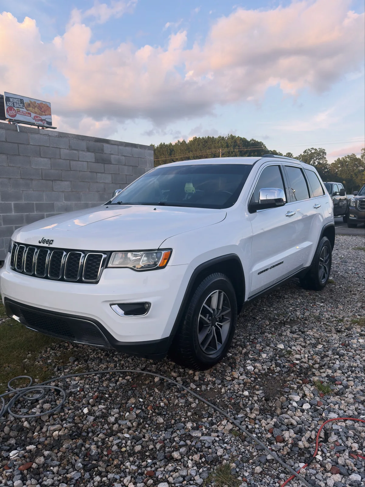 White Jeep Grand Cherokee Limited washed and shining on gravel at sunset